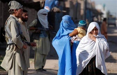 Pakistani women walk past armed men standing guard in Badaber situated in suburb of Peshawar, Pakistan, Wednesday, Feb. 25, 2009. <br/>(Photo: AP Images / Mohammad Sajjad)