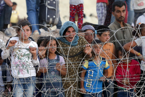 Syrian Kurds from Kobani wait behind the border fences to cross into Turkey as they are pictured from the Turkish border town of Suruc in Sanliurfa province, Turkey, June 25, 2015. Islamic State fighters have launched simultaneous attacks against Syrian government and Kurdish militia forces, moving back onto the offensive after losing ground in recent days to Kurdish-led forces near the capital of their 