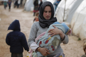 A woman carries a baby inside Al-Karameh refugee camp beside the Syrian-Turkish <br/>Reuters