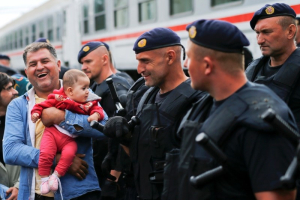 A migrant laughs as he holds a baby beside police at the train station in Tovarnik, Croatia, September 20, 2015. REUTERS/Antonio Bronic <br/>