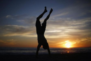 A man does a handstand as the sun sets over the Pacific Ocean on the beach in Santa Monica, California October 3, 2014.  <br/>REUTERS/Lucy Nicholson