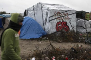 A migrants walks past a tent with a graffiti reading 