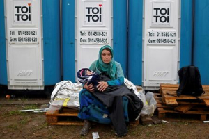 A woman carrying a child sits in front of portable toilets at a migrant camp in Opatovac, Croatia October 19, 2015.  <br/>REUTERS/Dado Ruvic