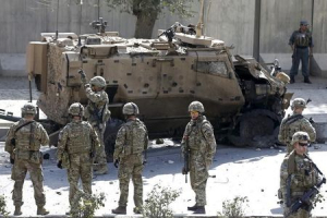 NATO soldiers stand near a damaged NATO military vehicle at the site of a suicide car bomb blast in Kabul, Afghanistan, October 11, 2015. <br/>Reuters
