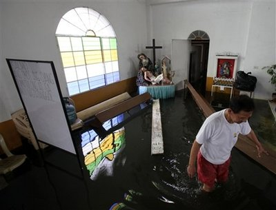 Juno Urbina, 68, a church caretaker, wades through a flooded San Roque church at Santa Cruz township, Laguna province, south of Manila, Philippines, Monday, Oct. 5, 2009. Typhoon Parma weakened into a tropical storm that lingered off the Philippine coast Monday, drenching northern provinces as well as Taiwan after killing people and causing widespread flooding and landslides. The sign at right reads: Psalm: God Helps and Defends. <br/>(Photo: AP Images / Bullit Marquez)