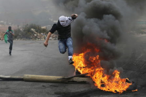 A Palestinian protester jumps past a burning tyre during clashes with Israeli troops during clashes near the Jewish settlement of Bet El, near the West Bank city of Ramallah October 27, 2015.  <br/>REUTERS/Mohamad Torokman