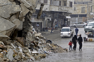 Civilians walk in the rain past a damaged building in the rebel-controlled area of Maaret al-Numan town in Idlib province, Syria October 28, 2015.  <br/>REUTERS/Khalil Ashawi