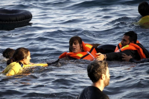 A volunteer lifeguard (L) helps a refugee as a half-sunken catamaran carrying around 150 refugees, most of them Syrians, arrives after crossing part of the Aegean sea from Turkey on the Greek island of Lesbos, October 30, 2015.  <br/>Reuters