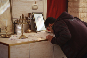 Assyrian Christians are trying to ward off extinction in Syria after Islamic State militants blew apart their villages. An Assyrian Christian man kisses a cross after taking communion in Tell Tamer, Syria. A photograph shows one of at least three people killed after ISIS took about 300 people captive in March 2015. <br/>NPR / Alice Ford