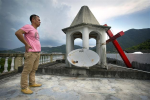 In this July 29, 2015 photo, lay leader Tu Shouzhe stands on his Protestant church's roof hours after Chinese government workers came and cut down the building's cross, at right, in Muyang Village in Pingyang County in eastern China's Zhejiang Province. Photo Credit: AP Photo <br/>