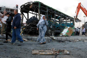People walk past a destroyed passenger bus hit by an ISIS bomb in the Syrian city of Jableh. <br/>Photo: Reuters