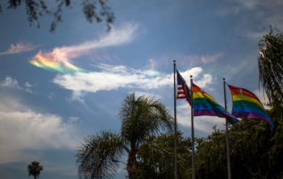 A rainbow is seen in the sky behind LGBT pride flags and the U.S. flag in West Hollywood, California, United States, June 26, 2015. <br/>REUTERS/Lucy Nicholson