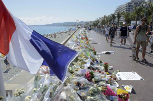 People walk past flowers left in tribute at a makeshift memorial to the victims of the Bastille Day truck attack near the Promenade des Anglais in Nice, France, July 21, 2016.<br />
 <br/>REUTERS/JEAN-PIERRE AMET