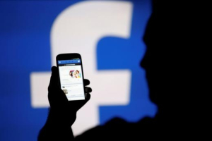 A man is silhouetted against a video screen with a Facebook logo as he poses with a Samsung S4 smartphone in this photo illustration<br />
<br />
 <br/>Reuters/Dado Ruvic 