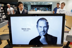 Customers look around products behind a computer monitor displaying the obituary of former Apple CEO Steve Jobs at an Apple Store in Seoul October 6, 2011. Apple Inc co-founder and former CEO Steve Jobs died on Wednesday at the age of 56, after a years-long and highly public battle with cancer and other health issues. <br/>REUTERS/Jo Yong-Hak
