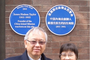Rev. Pong Lai and his wife standing in front of the two blue heritage plaques commemorating Hudson Taylor. <br/>Provided by author