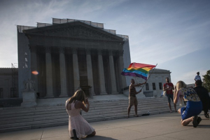 A demonstrator (back) waves a flag while awaiting decisions in two cases regarding same-sex marriage at the U.S. Supreme Court in Washington, June 26, 2013. America's top court was expected to deliver rulings on Wednesday in two high-profile cases with national implications on gay marriage, an issue that stirs cultural, religious and political passions in the United States as elsewhere. <br/>REUTERS/James Lawler Duggan