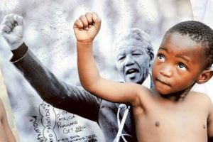 A young member of the Maitibolo Cultural Troupe poses in front of a photograph of Nelson Mandela outside the Medi Clinic Heart Hospital, where the anti-apartheid icon is admitted. <br/>AFP