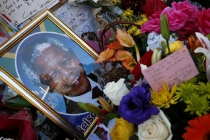 A well-wisher is reflected in the glass of a photograph left outside the hospital where ailing former President Nelson Mandela is being treated in Pretoria, July 16, 2013. Mandela turns 95 on July 18. REUTERS/Mike Hutchings <br/>