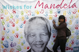 A well-wisher poses for a picture near a banner with the image of former South African President Nelson Mandela, outside the Medi-Clinic Heart Hospital where he is being treated, in Pretoria July 18, 2013. South Africa and the world showered tributes on Mandela on Thursday as the anti-apartheid leader turned 95 in hospital and his doctors reported he was ''steadily improving'' from a six-week lung infection. <br/>