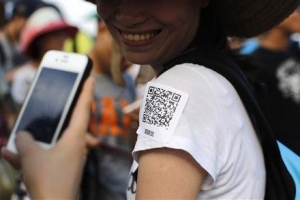 A man uses his phone to scan a QR code sticker, which is used to share personal information, during a matchmaking event in Jinshan beach, south of Shanghai July 20, 2013.  <br/>Reuters/Carlos Barria