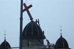 A crane winches a large red cross from one of three domes on the Guantou church in Wenzhou. The Chinese government has ordered the demolition of multiple churches around the country. <br/>
