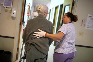 A program assistant at an adult care center helps her elderly patient. Cuts in cost-of-living adjustments impact retirees, making it more of a challenge to pay for health care services. (Justin Sullivan/Getty Images) <br/>