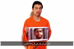 Kenji Goto is seen holding a picture of fellow hostage Mu'adh Safi Yusuf al-Kasasibah in the latest ISIS video. Photo: MEMRI <br/>